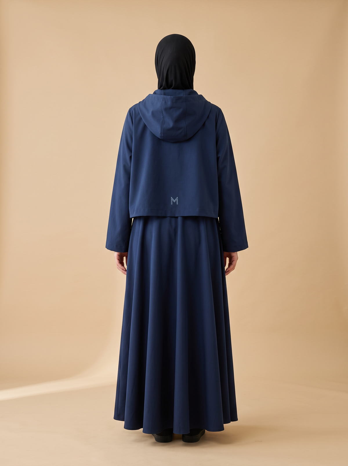 Sakina Layl, veste longue à capuche coloris bleu nuit, vue de dos, logo M brodé