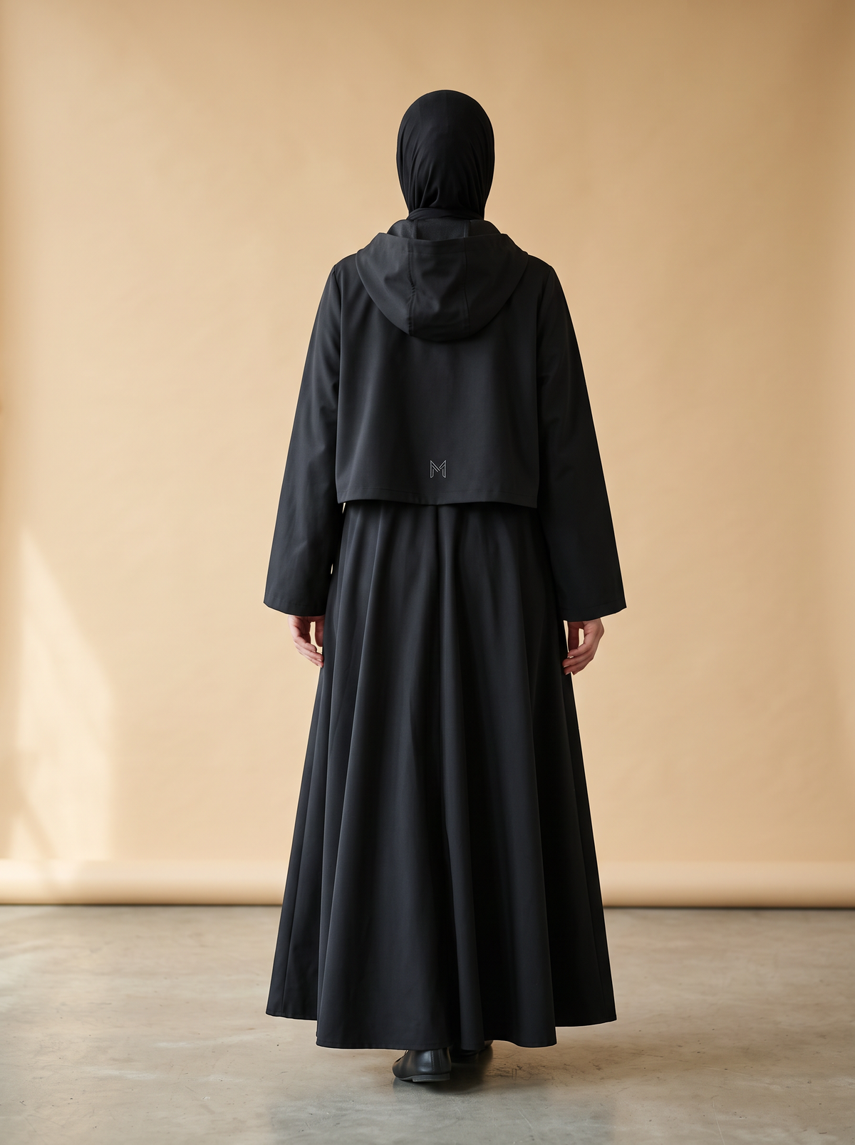 Sakina Kohl, veste longue à capuche coloris noir, vue de dos, logo M brodé